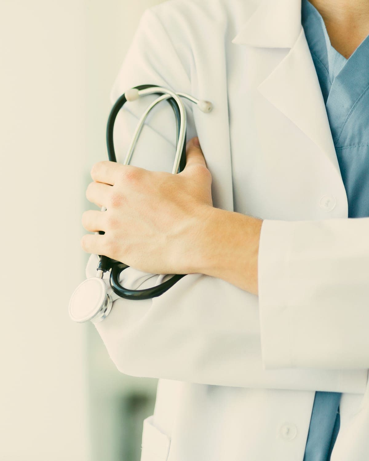 A nurse practitioner in a white coat and scrubs holding a stethoscope